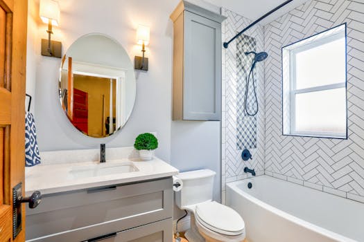 Servicios Elegant modern bathroom featuring chevron tiles, oval mirror, and sleek fixtures for a contemporary look.